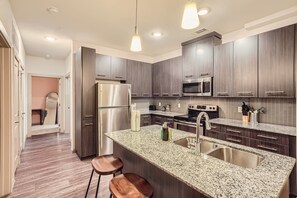 Une cuisine moderne avec des meubles en bois foncé, des appareils en acier inoxydable, des plans de travail en granit et des luminaires suspendus.
