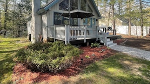A cabin with a large porch, surrounded by trees and a well-maintained garden. -  Cozy A-frame cabin just a short walk to town. (Ogunquit)