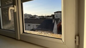 Une fenêtre donnant sur un ensemble d’immeubles, avec de nombreux toits visibles et un ciel dégagé.