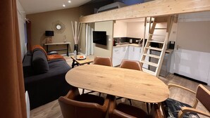 Un espace de vie compact comprenant un coin repas, un canapé, un téléviseur et un coin cuisine.