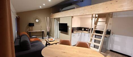 A compact living space with a dining area, a sofa, a TV, and a kitchen area.