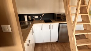 Une cuisine avec des meubles blancs, un escalier en bois et un plan de travail noir.