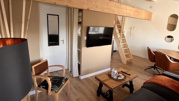 Un salon moderne avec un lit en mezzanine, un téléviseur à écran plat, des meubles en bois et un escalier menant à un niveau supérieur.