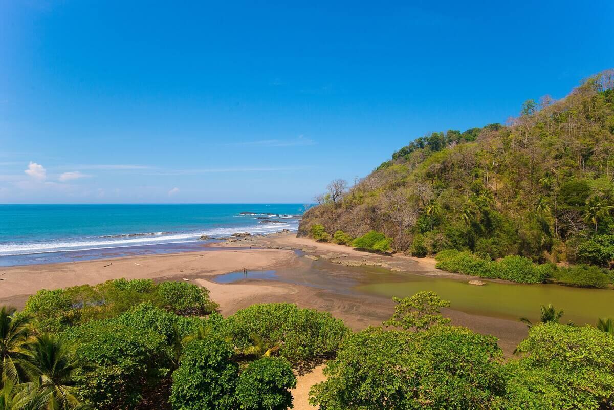 Un paisaje costero con playa, río y abundante vegetación.