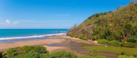 Un paisaje costero con playa, río y abundante vegetación.