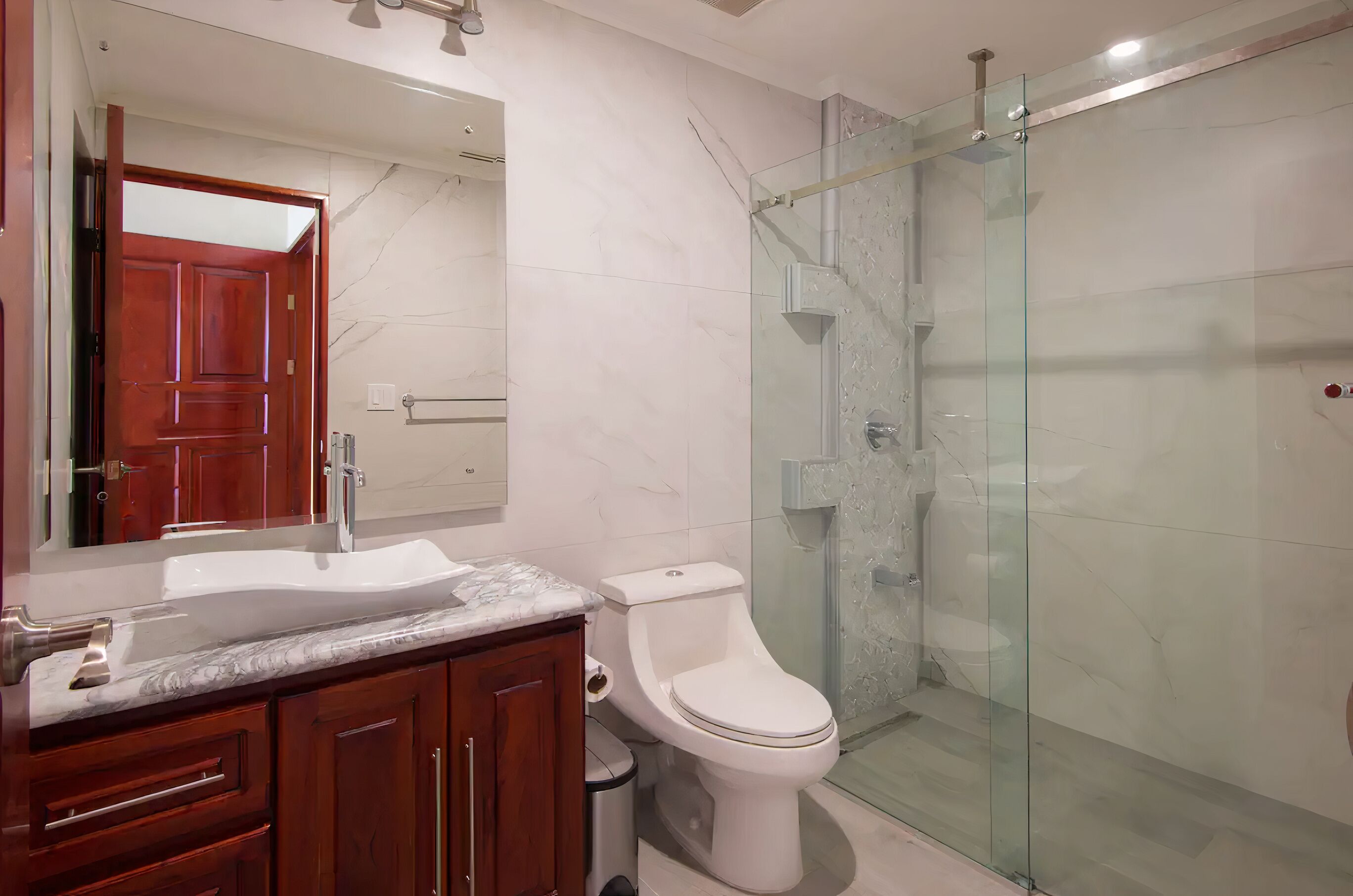 Een badkamer met een marmeren wastafel, houten wastafelmeubel, een wit toilet en een douche met glazen wanden.