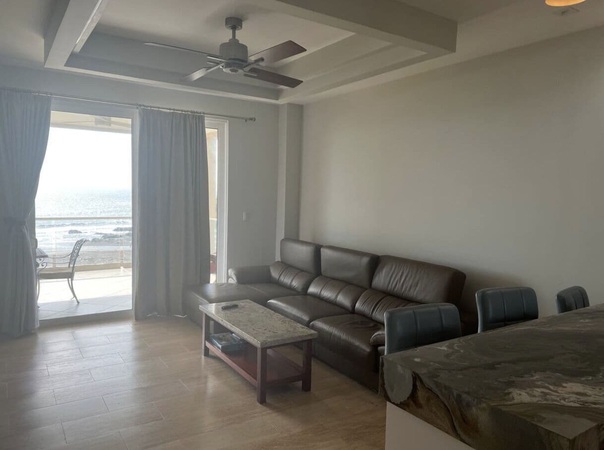 Una sala de estar con un sofá de cuero, una mesa de centro y vista al océano a través de amplios ventanales.