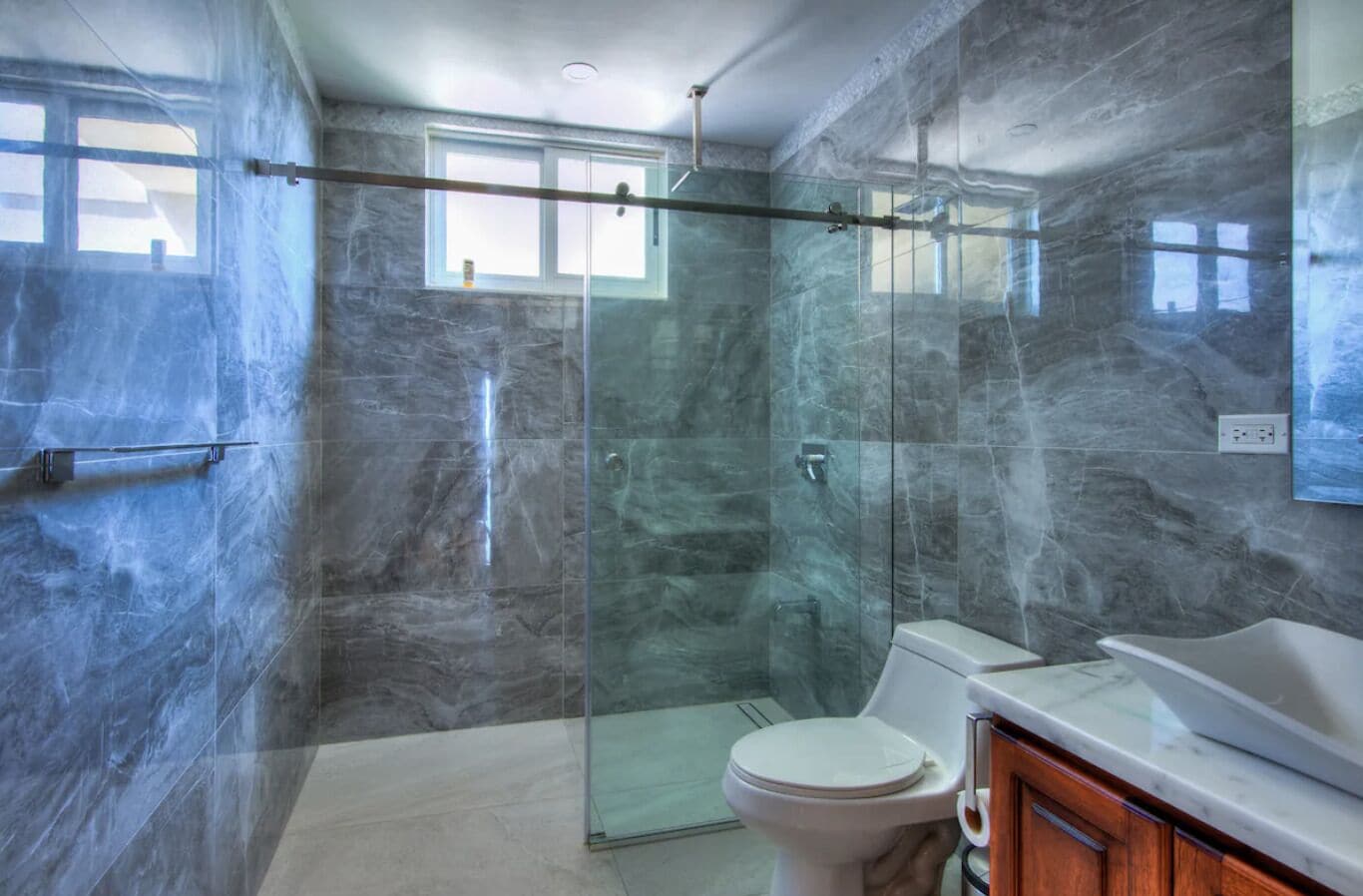 A modern bathroom with a glass-enclosed shower, a toilet, and a marble countertop.