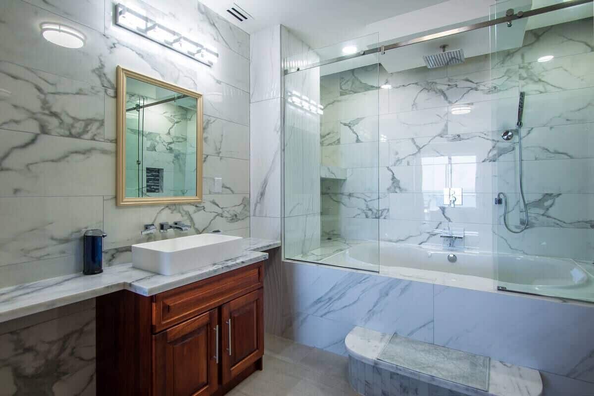 A modern bathroom with a marble vanity, a glass-enclosed shower, and a large mirror.