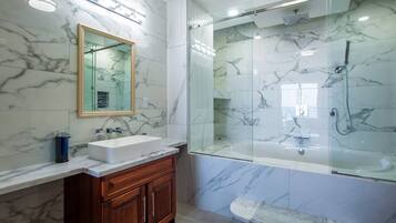 A modern bathroom with a marble vanity, a glass-enclosed shower, and a large mirror.