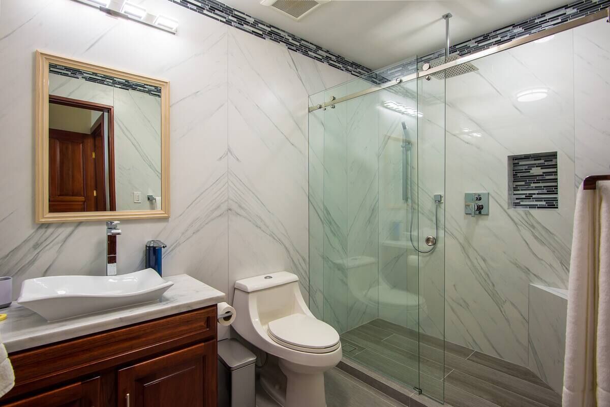 A modern bathroom with a glass shower enclosure, a marble-tiled wall, and a wooden vanity with a sink and mirror.