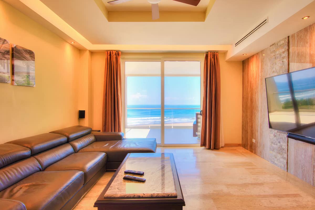 A modern living room with a leather sofa, a coffee table, and a large TV screen.