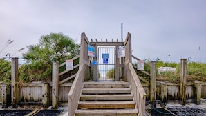 A wooden staircase leading to a gated entrance with signs and a blue informational sign.