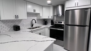 A modern kitchen with white cabinets, a stainless steel refrigerator, a black stove, and a white tiled backsplash.