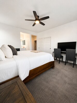 A bedroom with a bed, a desk, a chair, a ceiling fan, and a television.