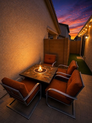 An outdoor patio with a table and chairs, a fire feature, and a view of a sunset.
