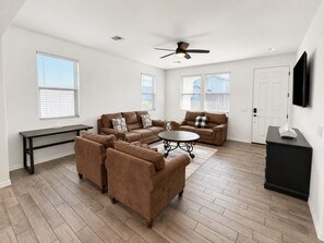 A spacious living room with a sofa set, a coffee table, and a TV mounted on the wall.