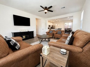 A modern living room with a flat-screen TV, leather sofas, a coffee table, and a ceiling fan.
