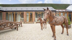 A building with a gravel driveway, wooden furniture, and two horse statues. - Stable Lodge Boutique B&B (Cheltenham)