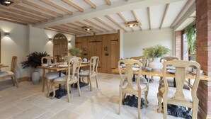 A dining area with wooden tables and chairs, a brick wall, and a large potted plant. - Stable Lodge Boutique B&B (Cheltenham)