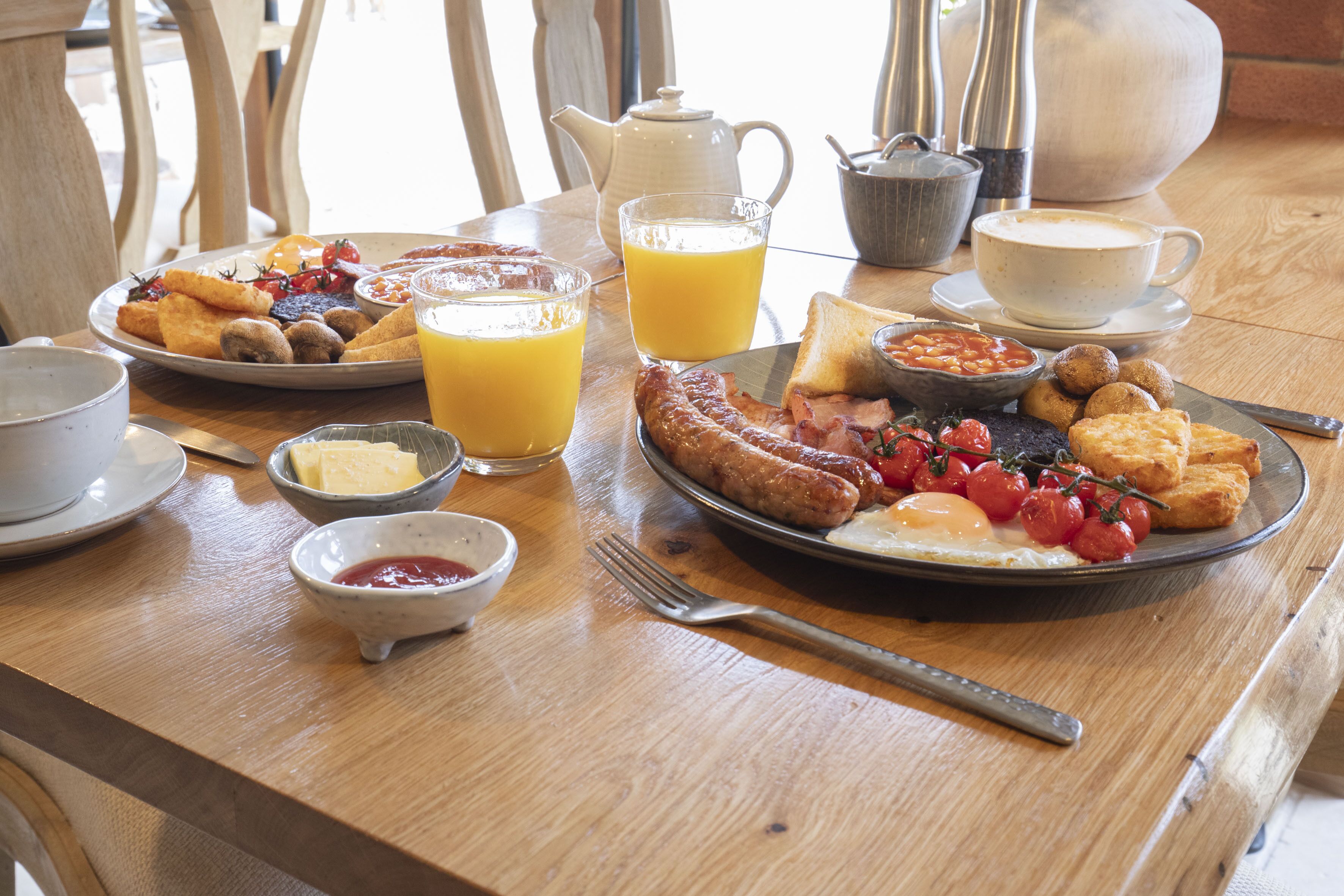 A breakfast table with plates of food, a teapot, a jug of orange juice, and a cup of coffee.