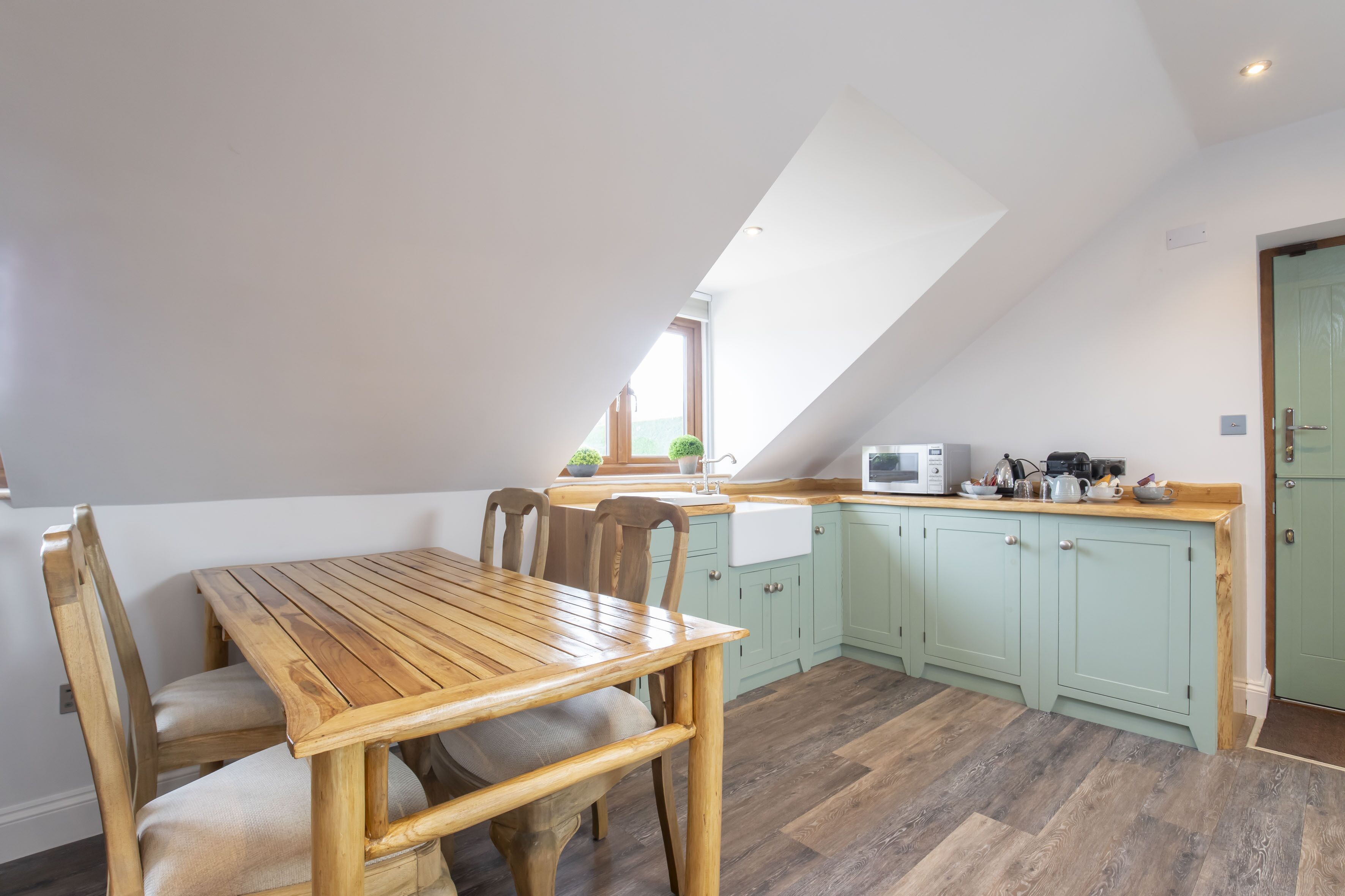 A kitchen with a wooden table and chairs, a window, and a microwave.