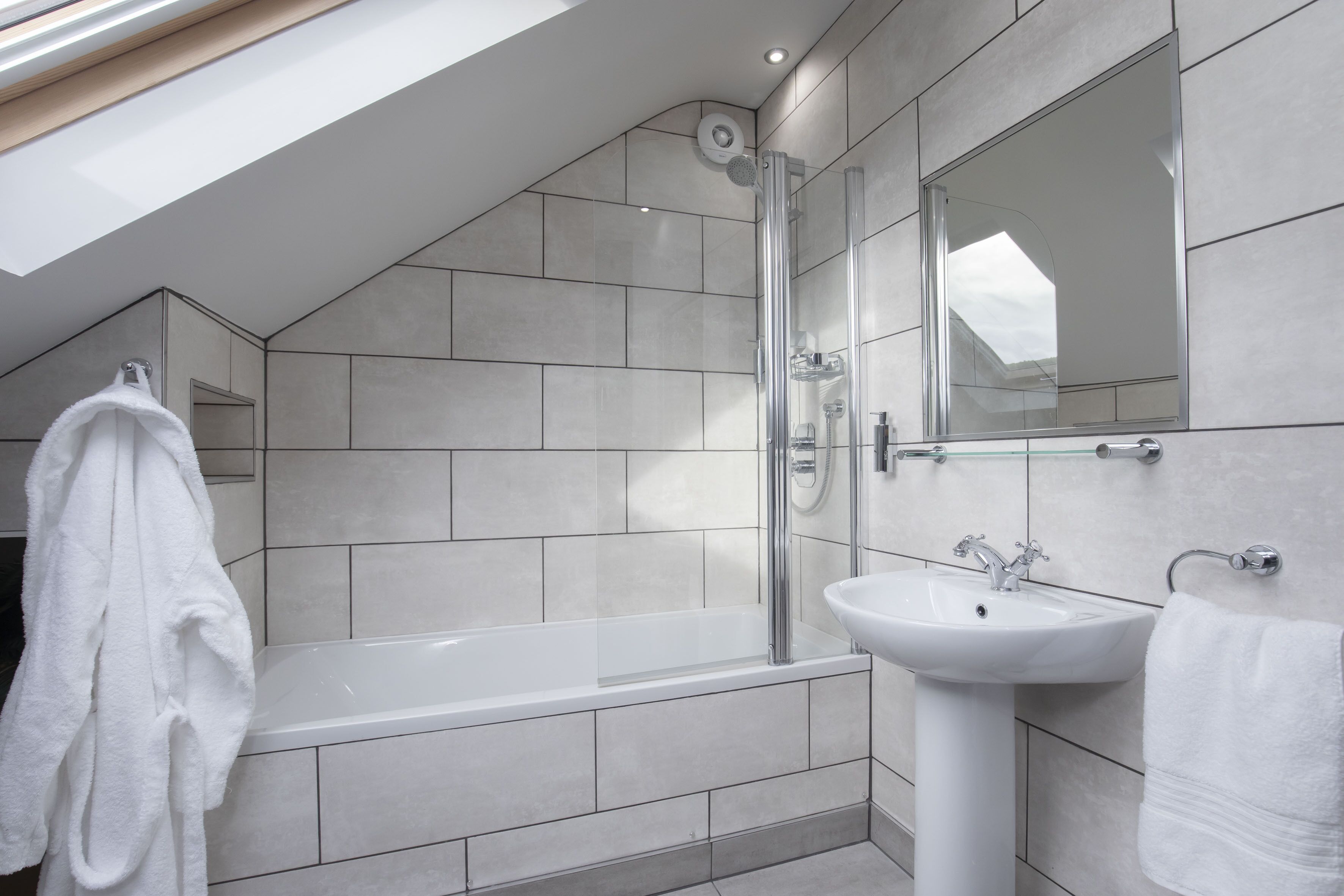 A modern bathroom with a skylight, a bathtub, a sink, and a large mirror.