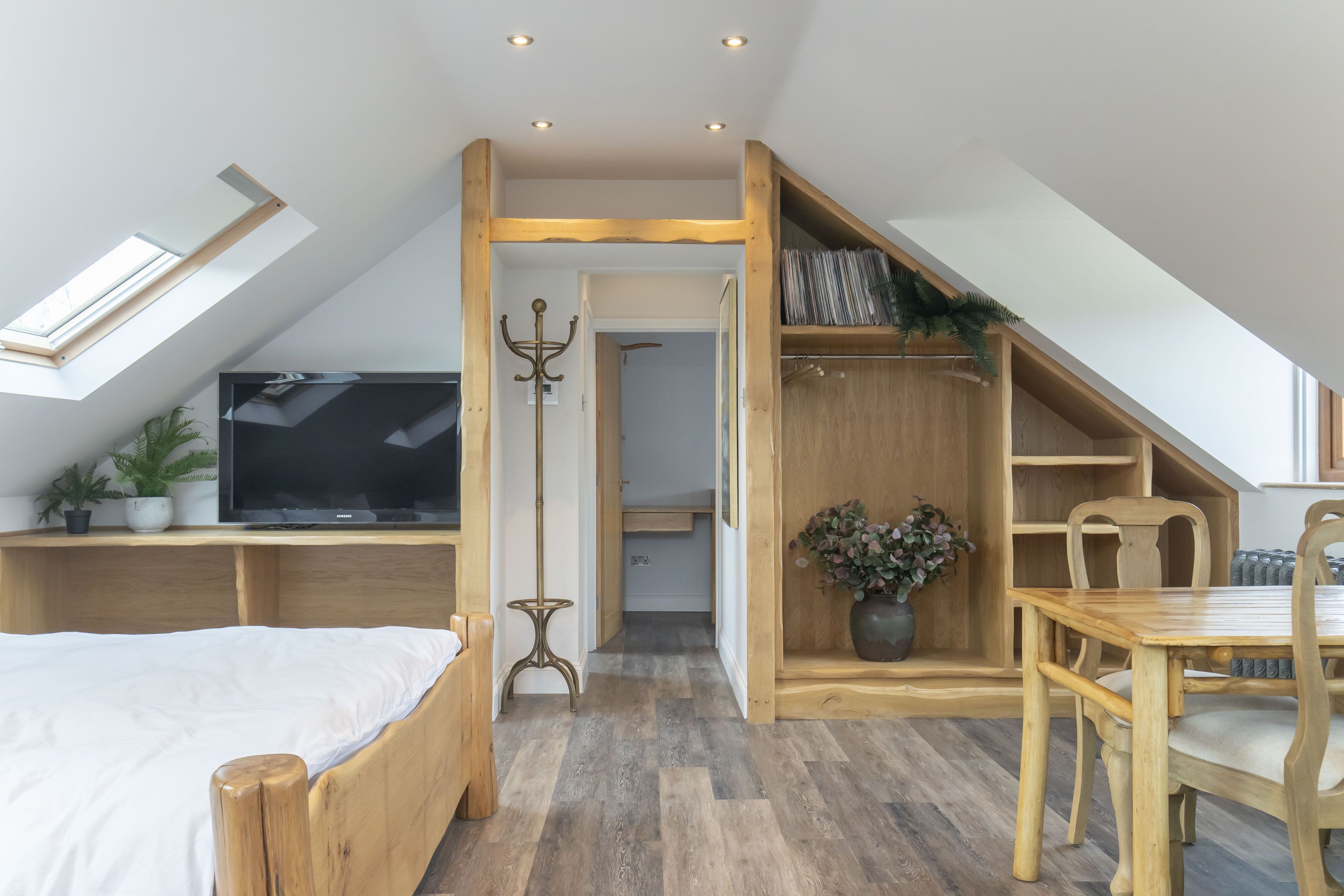 A loft-style bedroom with a sloped ceiling, a bed, a TV, a dining area, and a small seating space.