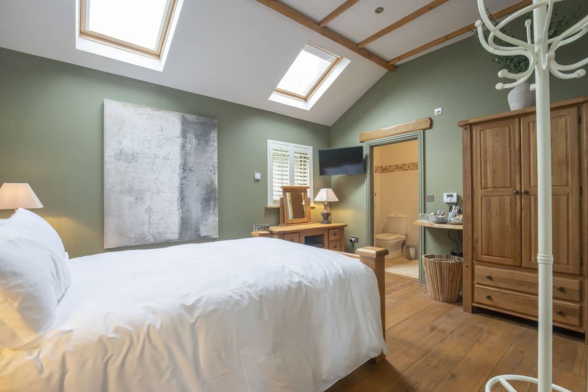 A bedroom with a skylight, a bed, a nightstand, a wooden cabinet, and a television.