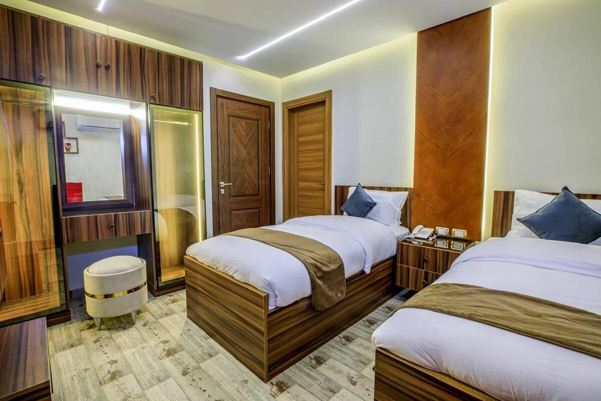 A hotel room with two beds, wooden paneling, a vanity with a mirror, and a small round table.