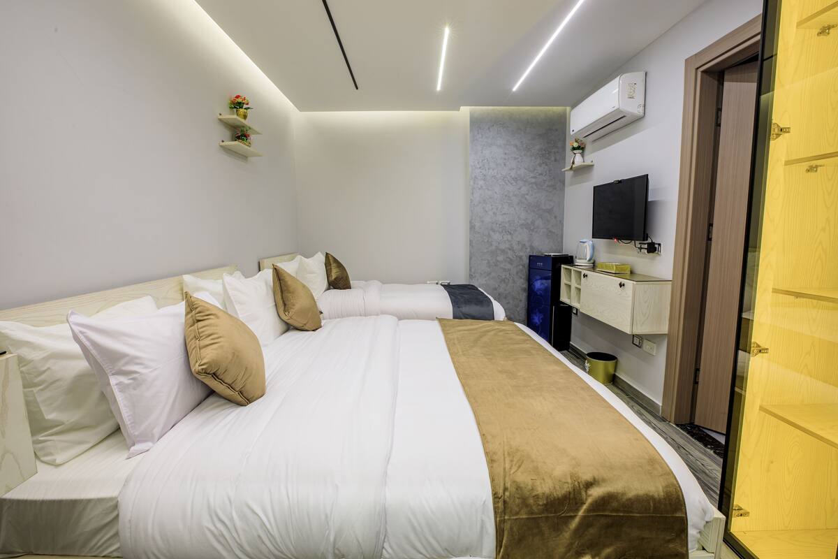 A modern hotel room with a large bed, a TV, a minibar, and a wooden wardrobe.