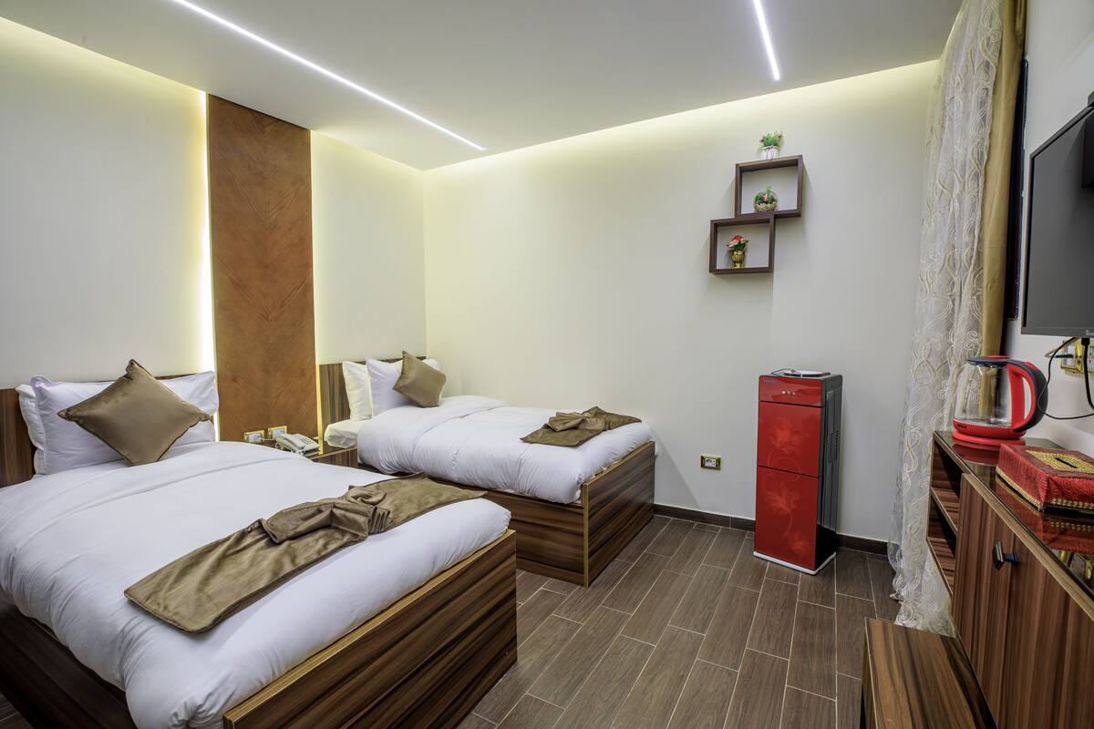 A hotel room with two beds, a red minibar, a TV, and a small shelf with decorative items.