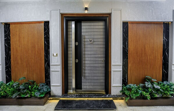 Una entrada moderna con una puerta oscura, paneles de madera verticales y detalles de mármol.