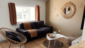 Un salon moderne avec un canapé foncé, un fauteuil en osier, une petite table blanche et un tapis tissé.