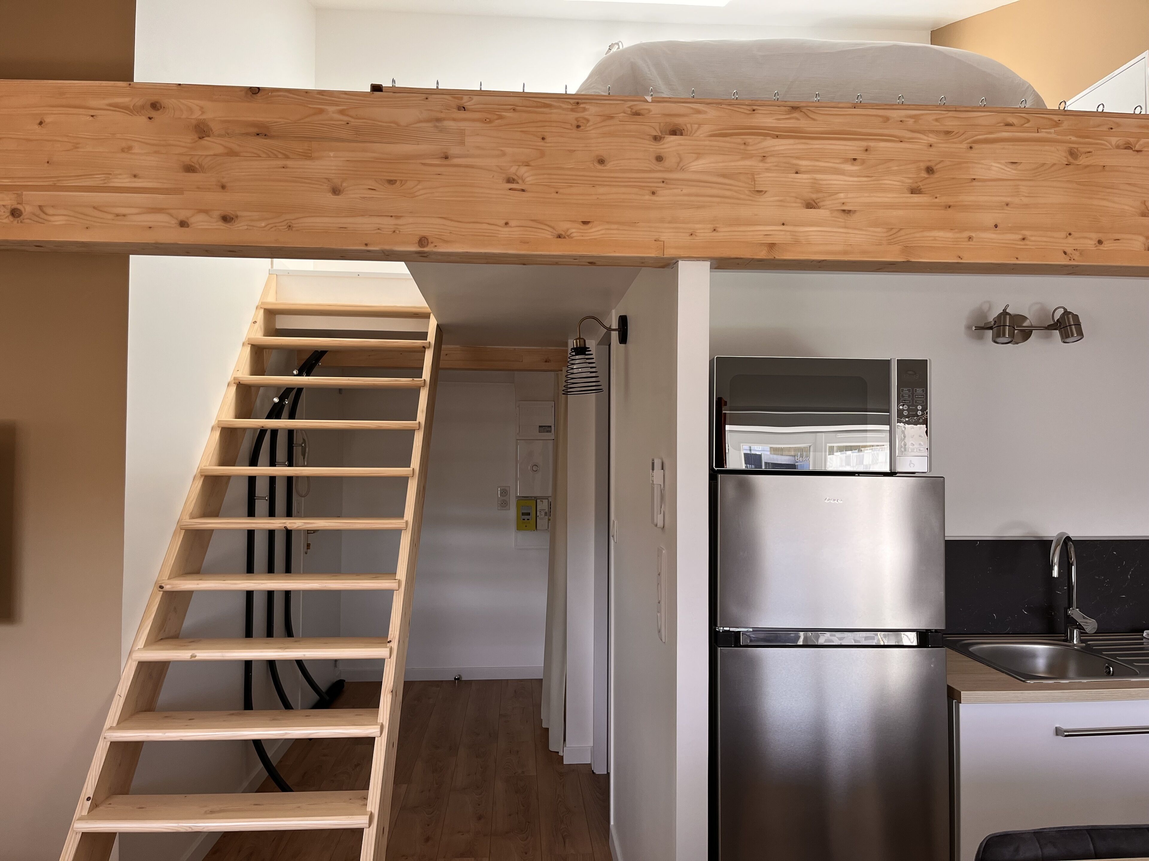 Une cuisine compacte dotée d’un réfrigérateur intégré et d’un escalier en bois menant à une chambre.