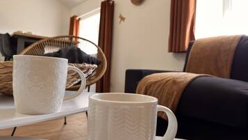 Un salon avec une table blanche, deux tasses blanches, un panier en osier, un canapé foncé et un chapeau marron accroché au mur.