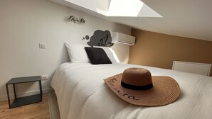 Une chambre à coucher comprenant un lit, une table de chevet, un climatiseur fixé au mur et un puits de lumière.
