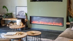 A modern living room with a fireplace, a sofa, a coffee table, and a TV mounted on the wall. - Luxury 6p. villa in Gaasterland near the woods and close to the (kite)beach. (Rijs)