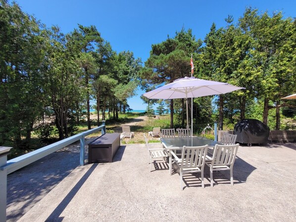 An outdoor patio with a table and chairs, a grill, and a view of the sea.