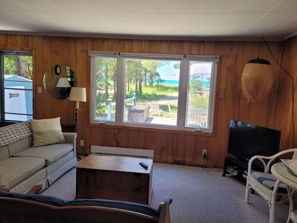 A living room with a sofa, a television, a table, and a window with a view of a beach.