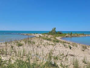 Paisagem costeira com praia arenosa, água azul cristalina e vegetação rasteira.