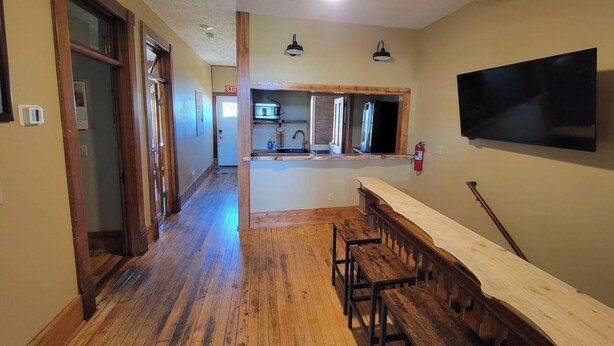 A spacious hallway with wooden flooring, a dining area with a long table and benches, a kitchen area with a microwave and sink, and a ceiling fan. - Experience history of brothel, 4 bedrooms, 6 min from attractions. Pets friendly (Custer)