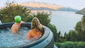 Two people in a hot tub with a scenic view of a lake and mountains in the background.