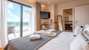 A modern hotel room with a large bed, a TV mounted on the wall, a balcony with a chair, and a bathroom visible through an open door. - Beautiful home in Kastelir with sauna (Kastelir)