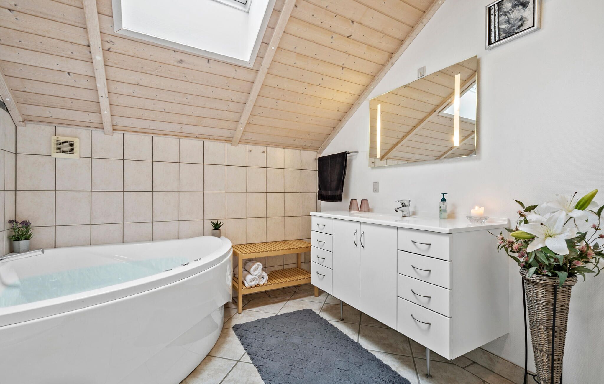 Un baño moderno con una bañera independiente, un tocador con cajones, un espejo y una planta de mimbre.