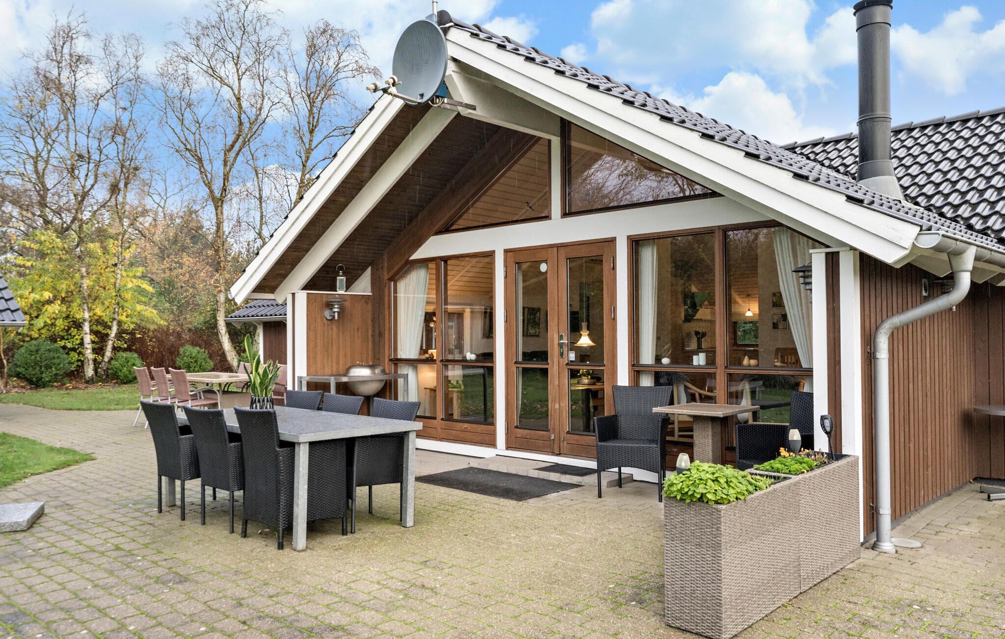 A modern building with a sloped roof, large windows, and outdoor seating area with tables and chairs.