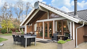 A modern building with a sloped roof, large windows, and outdoor seating area with tables and chairs. - Awesome home in Ulfborg with kitchen (Ulfborg)