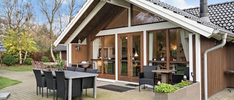 A modern building with a sloped roof, large windows, and outdoor seating area with tables and chairs.