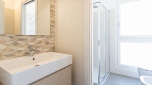 Un baño con lavamanos blanco, cabina de ducha de vidrio y ventana que proporciona luz natural.