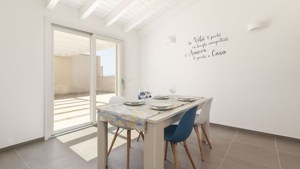 Un comedor con una mesa dispuesta para dos personas, un puerta corrediza de vidrio que da a un espacio exterior y una pared con una cita inspiradora.